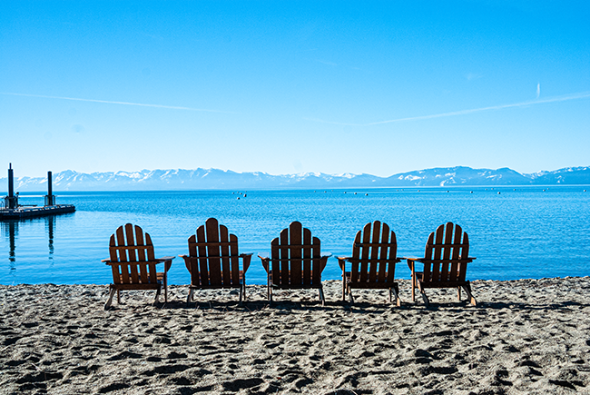 Liegestuehle am Strand von Lake Tahoe mit verschneiten Bergen im Hintergrund